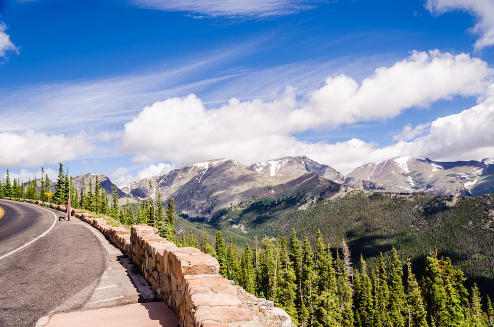 Views from the rainbow curve on the trail ridge road in Rocky Mountain National Park, including mountains, trees, and a blue cloudy sky.