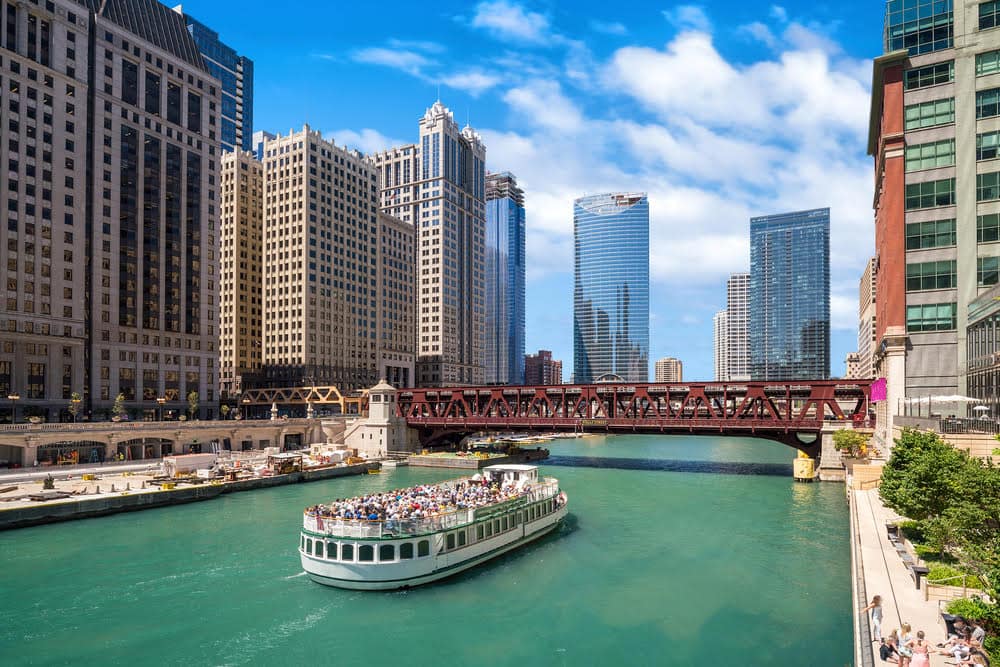 A boat floating on a river through Chicago with the skyline in the background - one of the best place to visit in the USA in March.