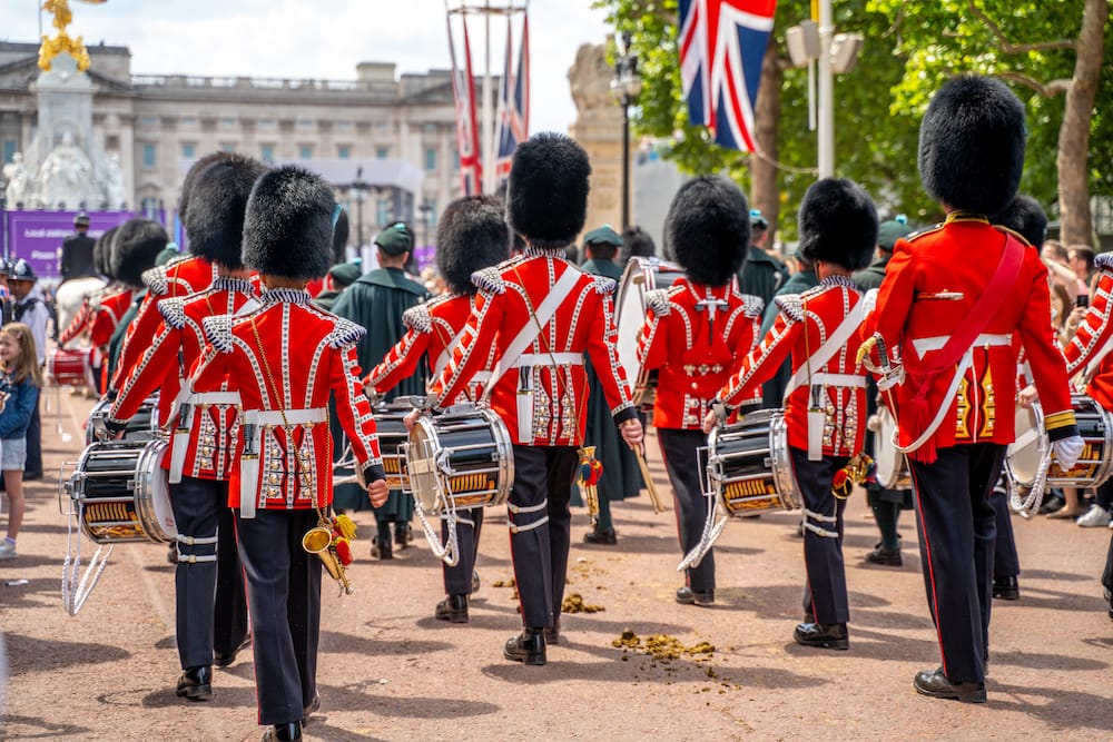 Several soldiers in red coats and black hats marching with their drums during the Changing of the Guard at Buckingham Palace – one of the best cheap things to do in London.