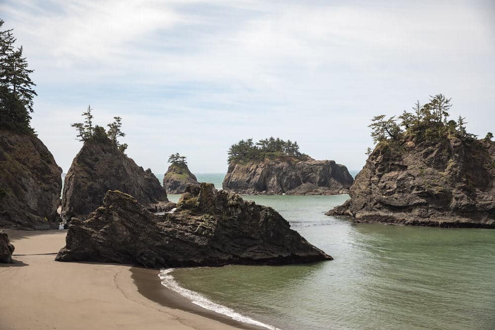 Several rocks with trees on them sitting in the ocean on a beach on the Oregon Coast, one of the best places to visit in the USA in July
