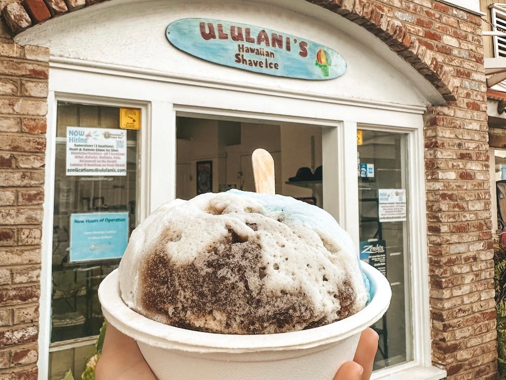 A blue, white, and brown shave ice in front of Ululani's Hawaiian Shave Ice, one of the best places to eat in Maui.
