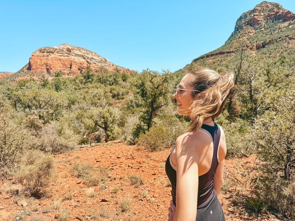 A woman in a black hiking tank top standing in front of the red rocks in Sedona on the Devil's Bridge Hike, one of the best things to do in Sedona