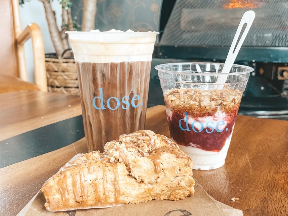 A large iced coffee with cold foam, a yogurt parfait, and a scone in front of a fireplace on a wooden table at Dose, one of the best coffee shops in Nashville