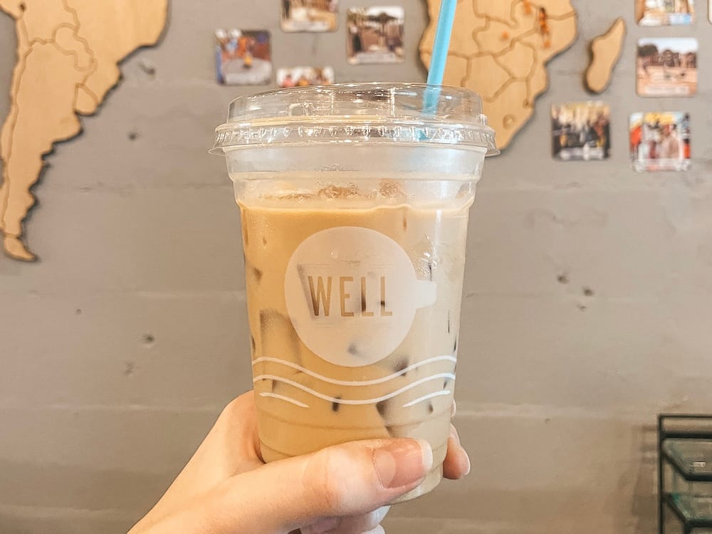 An iced coffee in front of a wall with a wooden map and photos from The Well, one of the best places to get coffee in Nashville