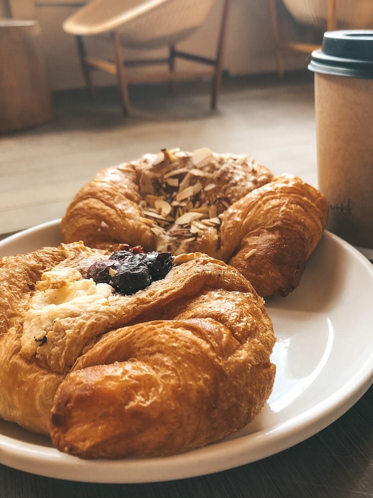 Two croissants are sitting on a white plate on a wooden table.