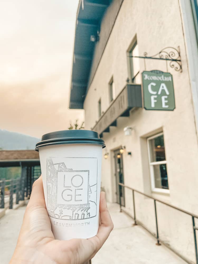 A hand holding a cup of coffee in front of a building at sunrise.