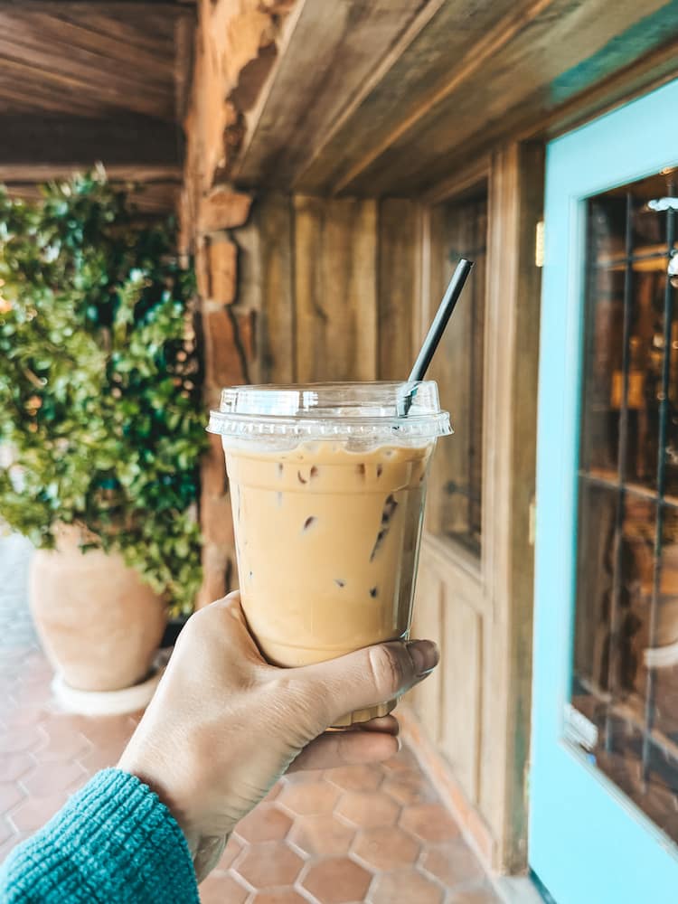 A woman in a green sweater holding an iced coffee in front of a wood building in Sedona