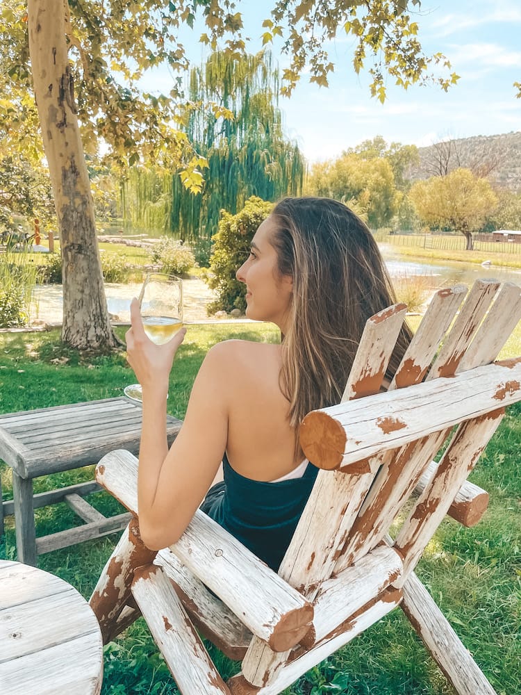 A woman sitting in a wooden chair overlooking a lake with a glass of wine in hand at one of the best wineries in Sedona