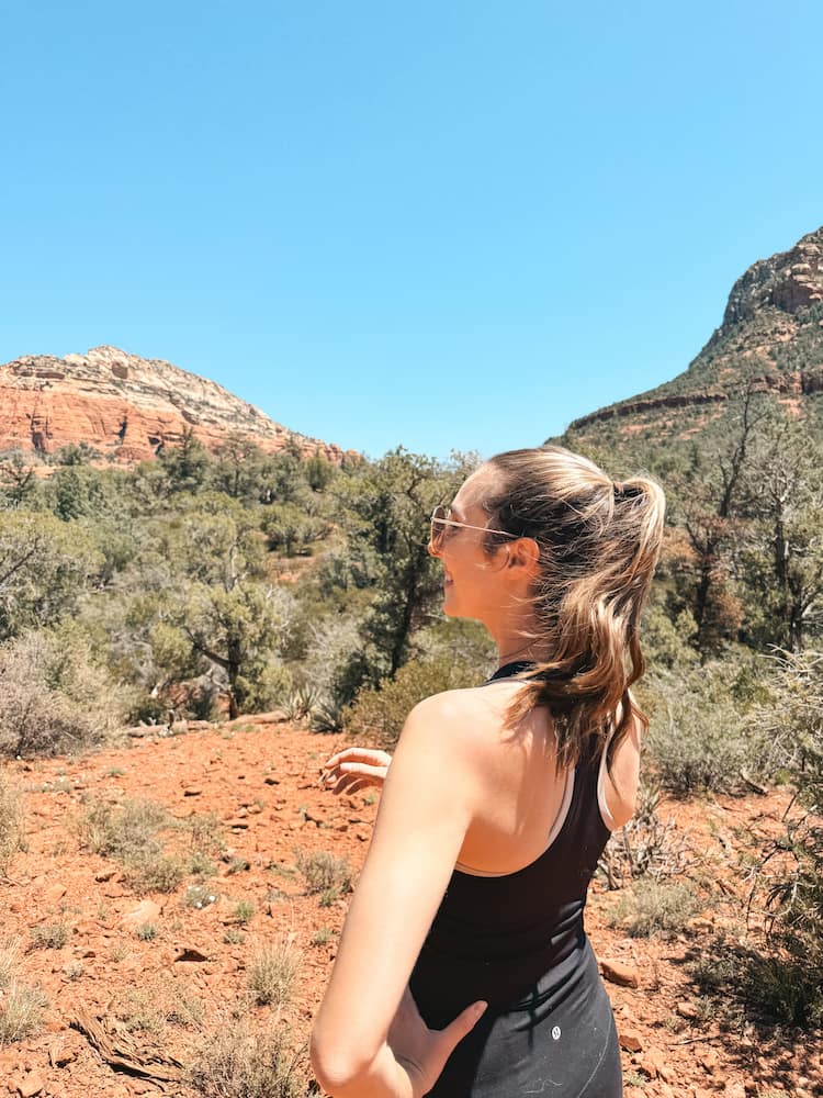 A woman with a brown ponytail and a black workout outfit standing on a hiking trail in Sedona