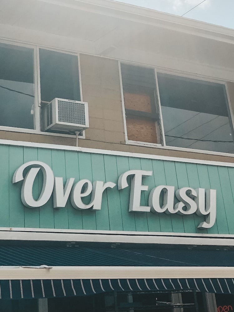 A sign that says Over Easy on wood that is painted green on a building in Hawaii.