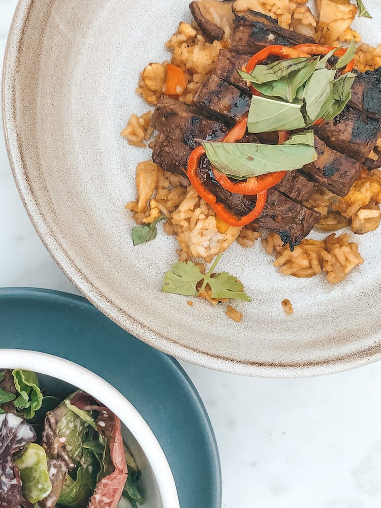 A salad and a dish with rice, meat, and veggies sitting on a white table in Coronado Island.