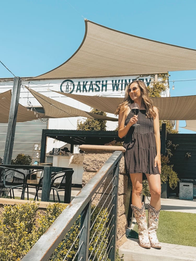A woman in a black sundress with white cowboy boots standing in front of Akash Winery in Temecula