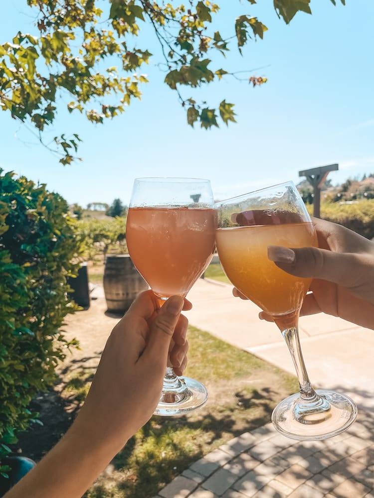 Two glasses of sangria being clinked together in front of a lush winery in Temecula.