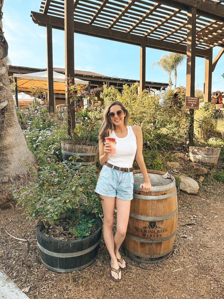 A woman in denim shorts and a white tank top holding a wine slushy at one of the best wineries in Temecula