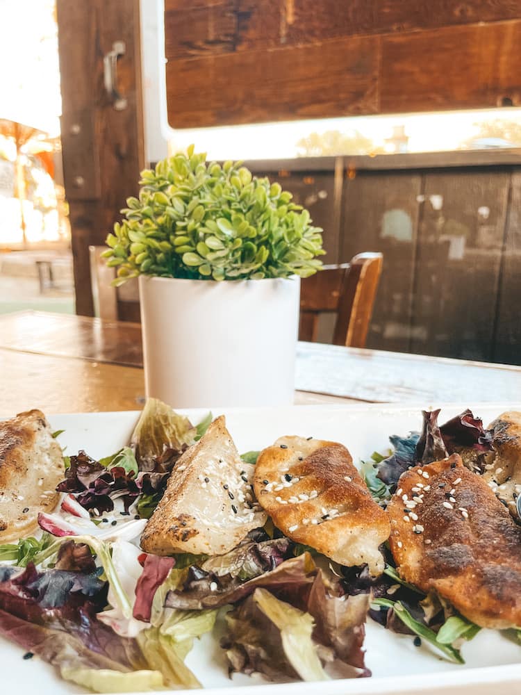 A plate of empanadas sitting on a wooden table in front of a plant at a gastropub in Old Town Temecula.