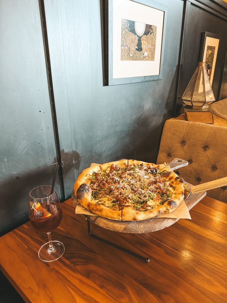 A wood-fired pizza and a glass of sangria sitting on a wooden table at a high-end restaurant in Old Town Temecula