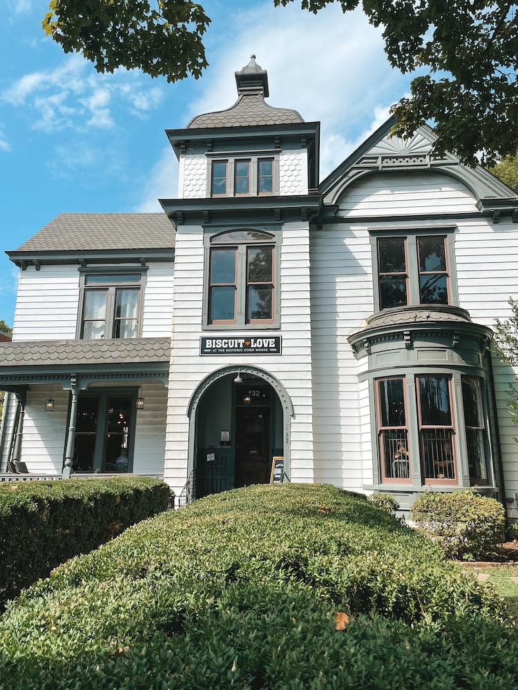 The Victorian-style exterior of Biscuit Love in Franklin with white siding and a black shingle roof behind a green bush