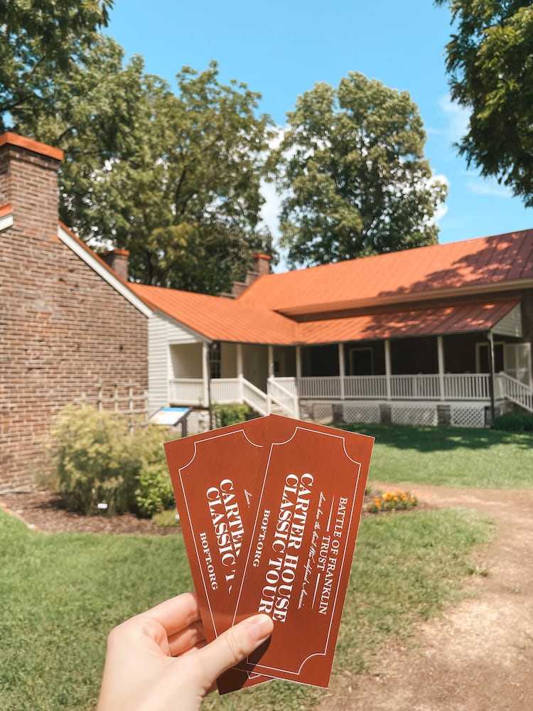 Two red tickets to the Carter House, an important Civil War site in Franklin, being held in front of the historic house