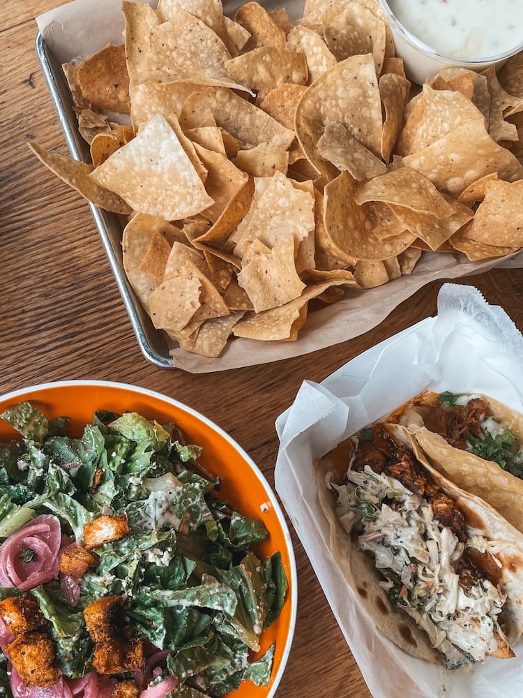 A salad, two tacos, and a plate of chips and queso sitting on a wooden table at Mojo's Tacos, one of the best places to eat in Franklin