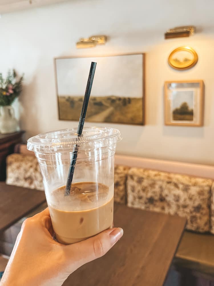 An iced coffee in a to-go cup inside a restaurant with vintage-style booths, wooden tables, and vintage decor.