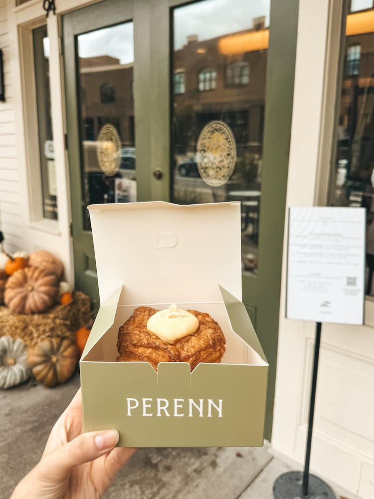 A pastry in a green to-go box in front of the doors of Perenn, one of the best bakeries in Franklin, with pumpkins and a hay bale sitting next to the door.