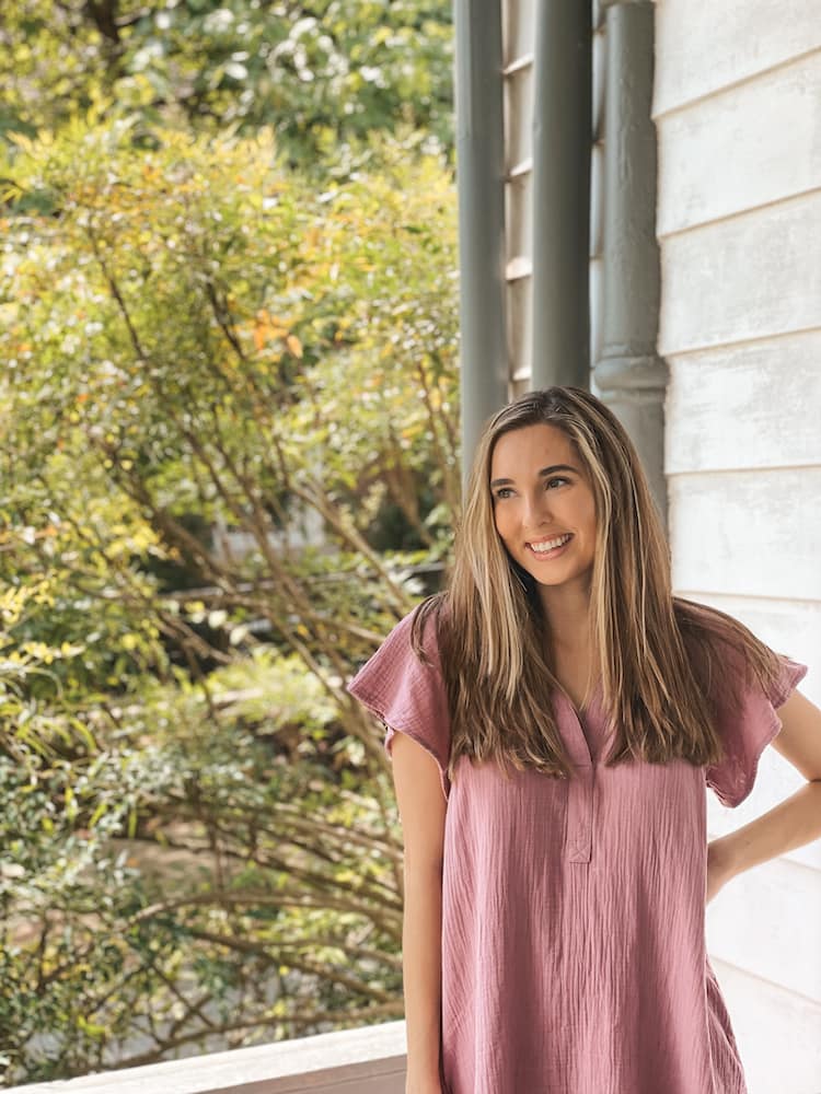 A woman in a purple dress standing on the porch of a historic building in Franklin, with lush greenery in the background