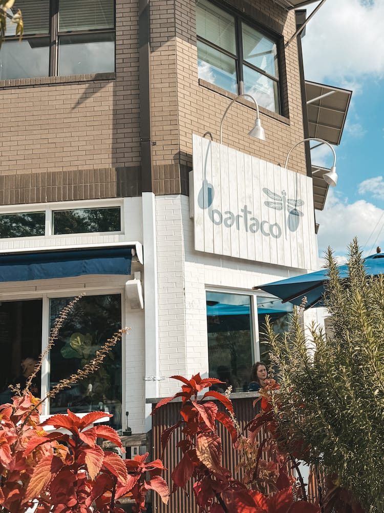 The white and blue sign for Bartaco in 12 South, surrounded by green and red plants and blue umbrellas