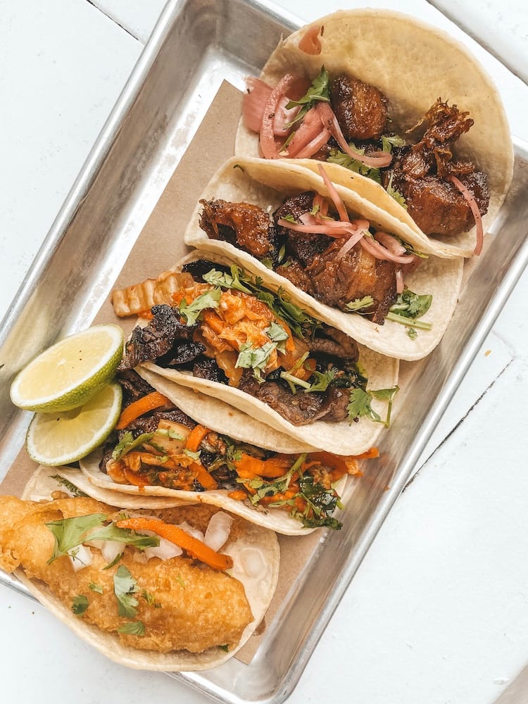 A metal tray of five street tacos sitting on a white wooden table at a restaurants in 12 South