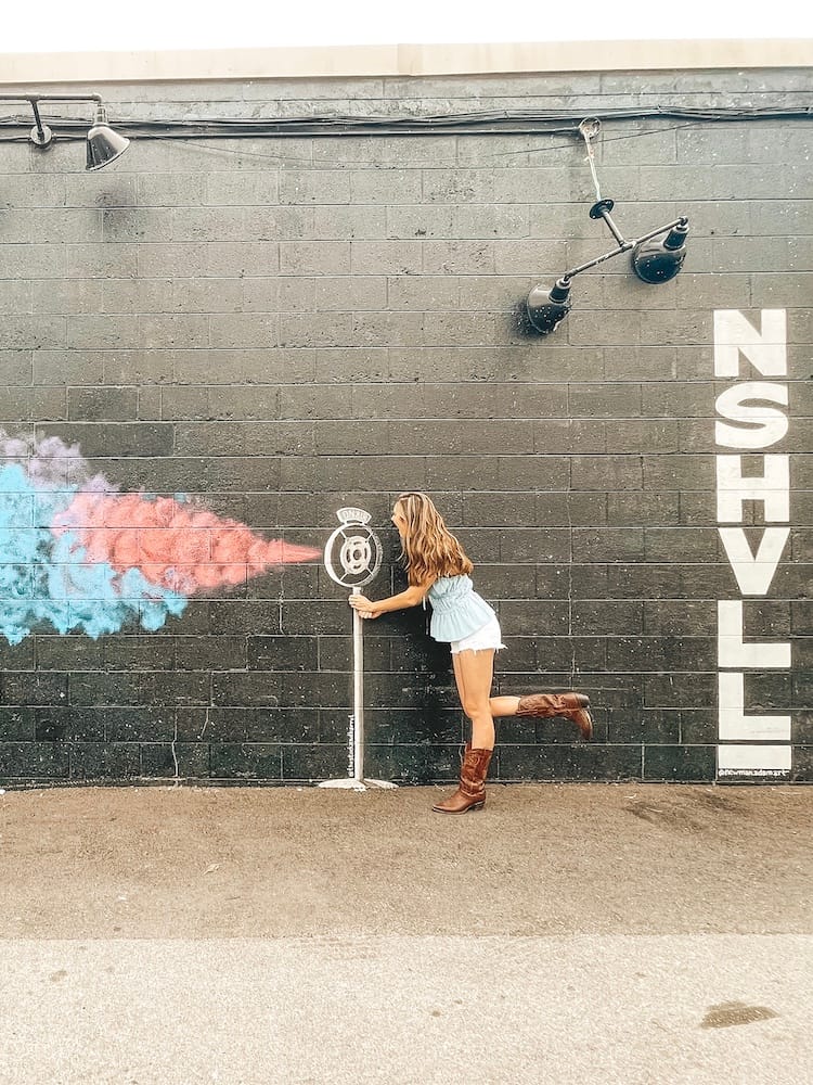 A woman wearing a blue tank top and white shorts "singing" into a microphone mural in The Gulch in Nashville