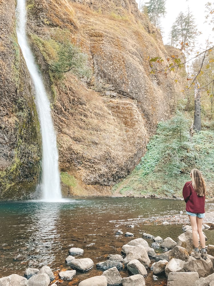A woman standing in a red sweatshirt in front of a waterfall in the Columbia River Gorge