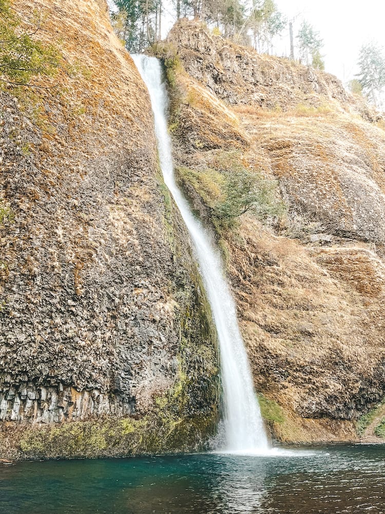 A waterfall cascading down a mountain and into a blue pool.