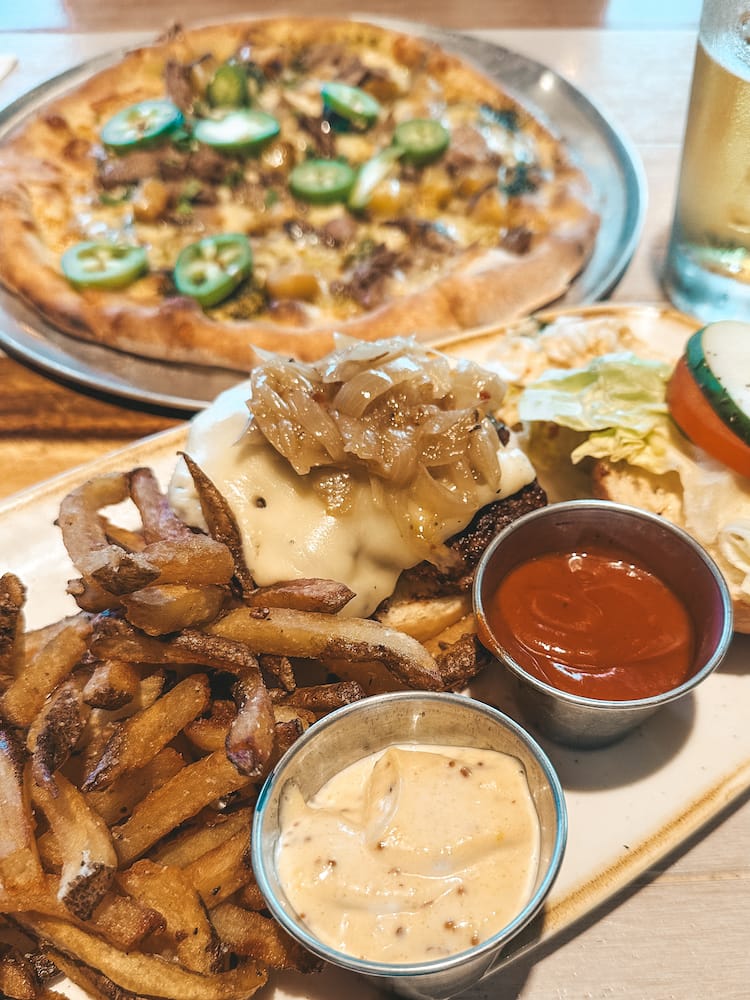 A burger and a pizza sitting on a wooden table at Monkeypod Kitchen in Maui.