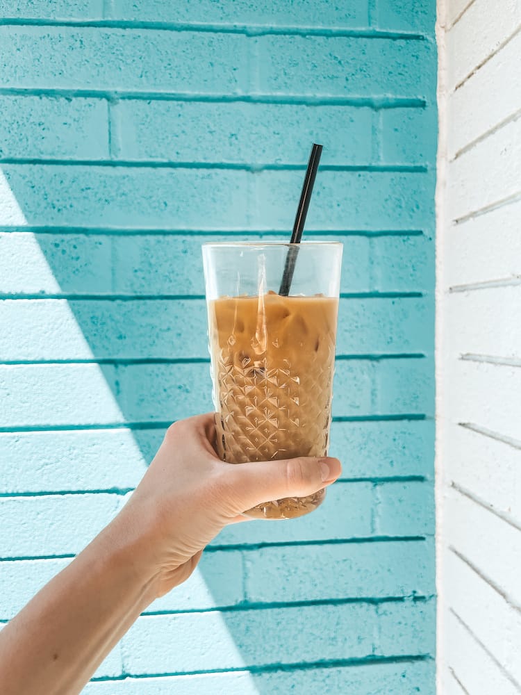 An iced coffee in a glass in front of a brick wall painted blue and white at The Eleanor in Old Town Scottsdale