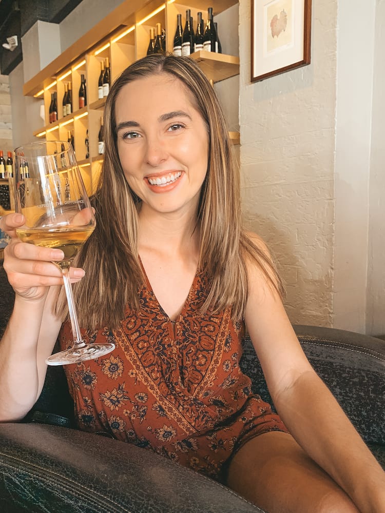 A woman with brown hair wearing an orange romper holding a glass of white wine at a wine tasting room in Old Town Scottsdale.