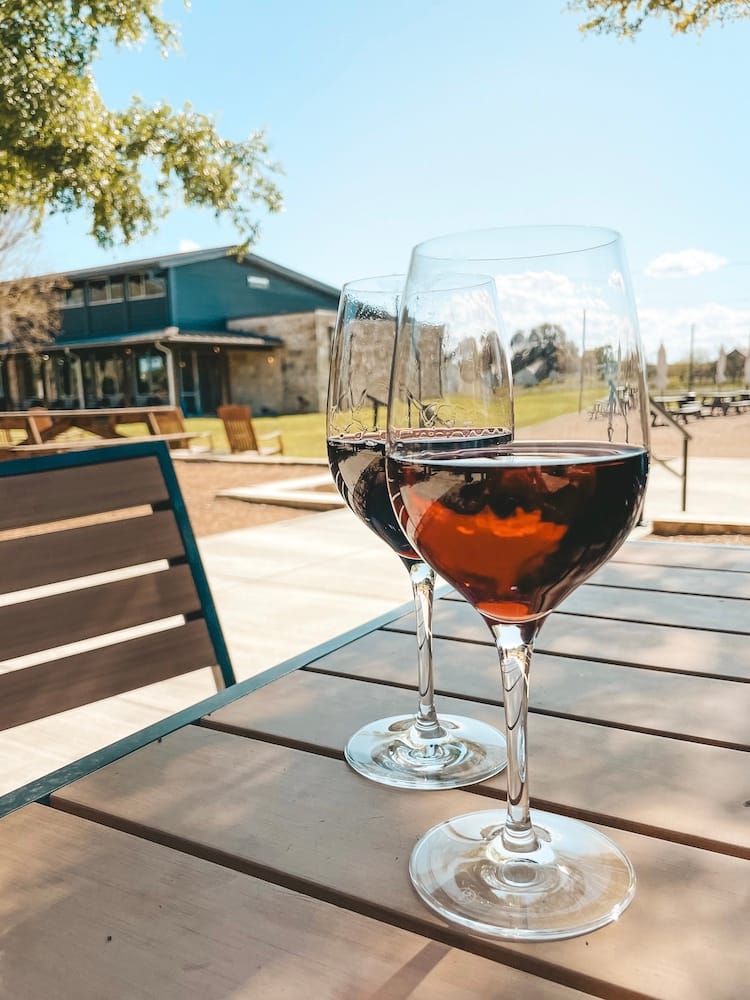 Two glasses of red wine sitting on a wooden table at a winery in Fredericksburg, TX