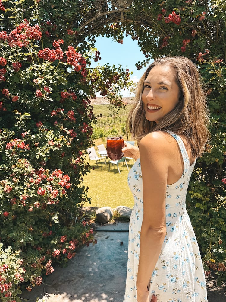 A woman holding a glass of red sangria in front of a greenery and flower arch at Alcantara Vineyards, one of the best wineries in Sedona