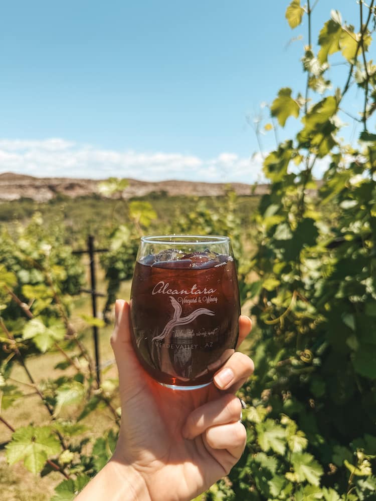 A glass of red sangria in front of the lush vineyards and mountains at Alcantara Vineyards, one of the best wineries and top things to do in Sedona