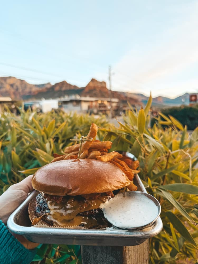 A tray with a burger, fries, and ranch being held in front of the red rocks in Sedona