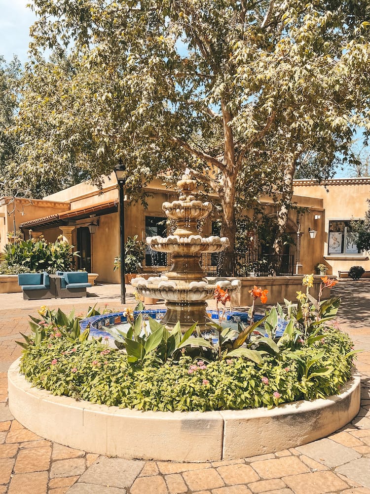 A fountain inside the Tlaquepaque Arts & Shopping Village in Sedona, with lush greenery and colorful flowers at the base of the fountain.