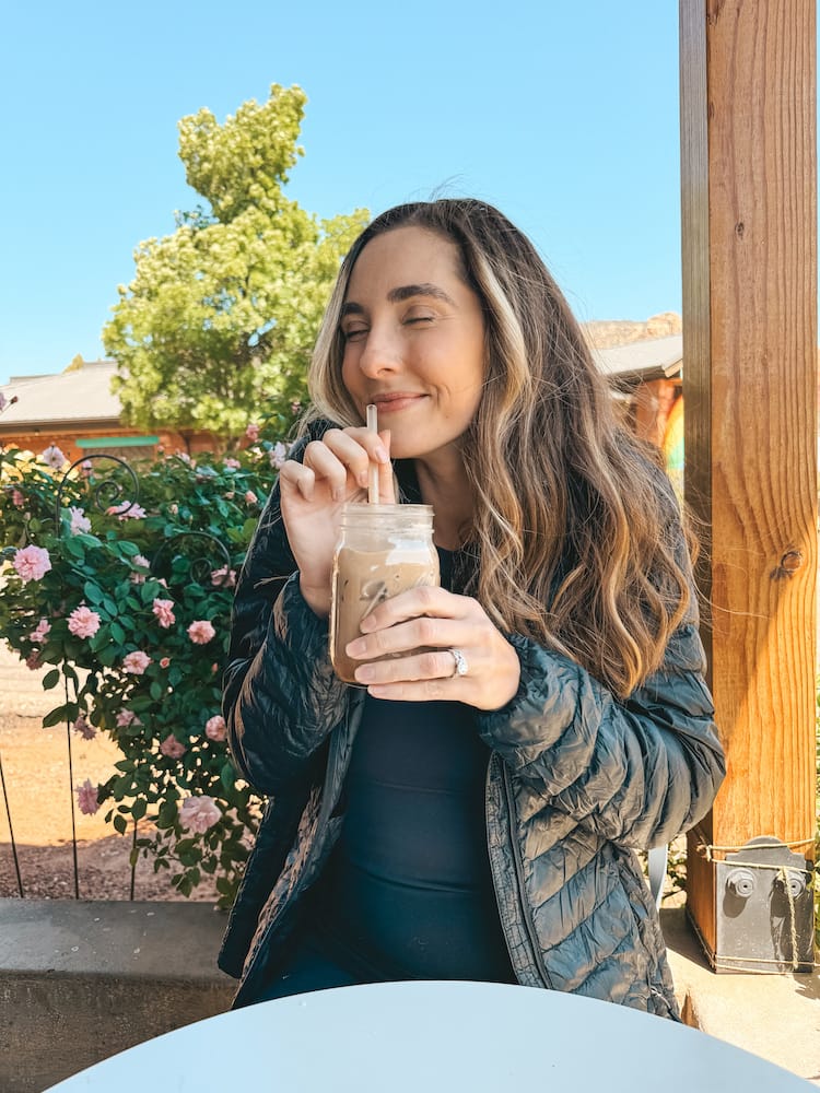 A woman in a black puffer jacket holding up an iced coffee at one of the best coffee shops in Sedona.