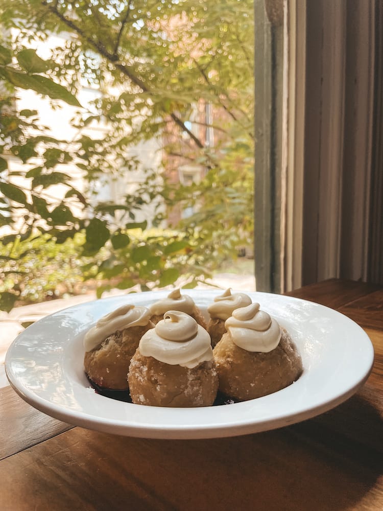 Five donut holes made from biscuit dought sitting on a plate on a table in front of a window with greenery outside.