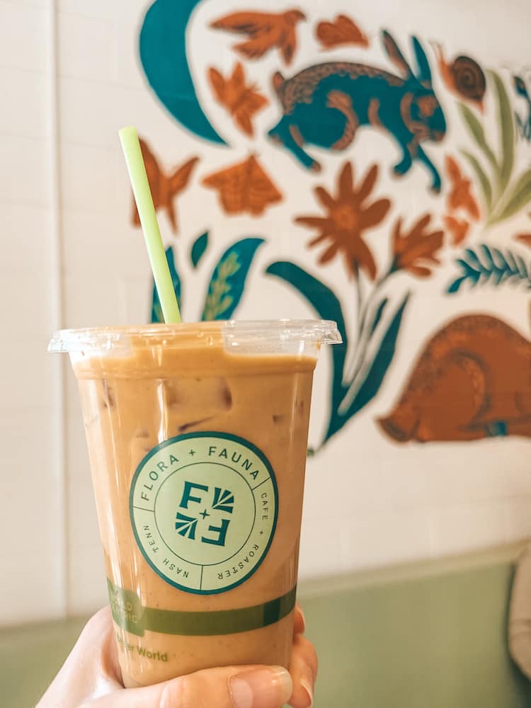 An iced coffee in front of a white wall with a mural of bunnies and flowers painted on it from Flora + Fauna Coffee in Nashville