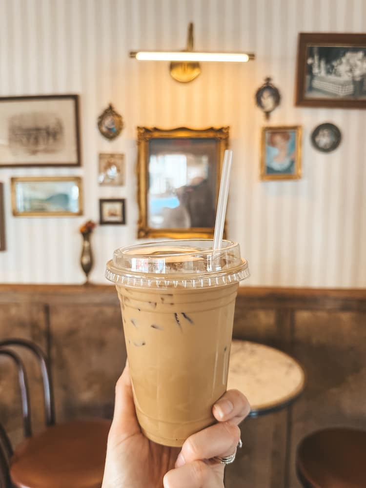 A cup of iced coffee in front of a wall with striped wallpaper and antique frames and vintage photos from Hank's Coffee Station, a popular coffee shop in Franklin