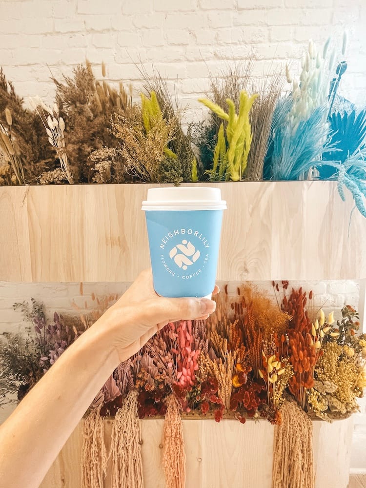 A blue cup of hot coffee in front of a flower display in Neighborlily, a coffee and floral shop in Germantown in Nashville