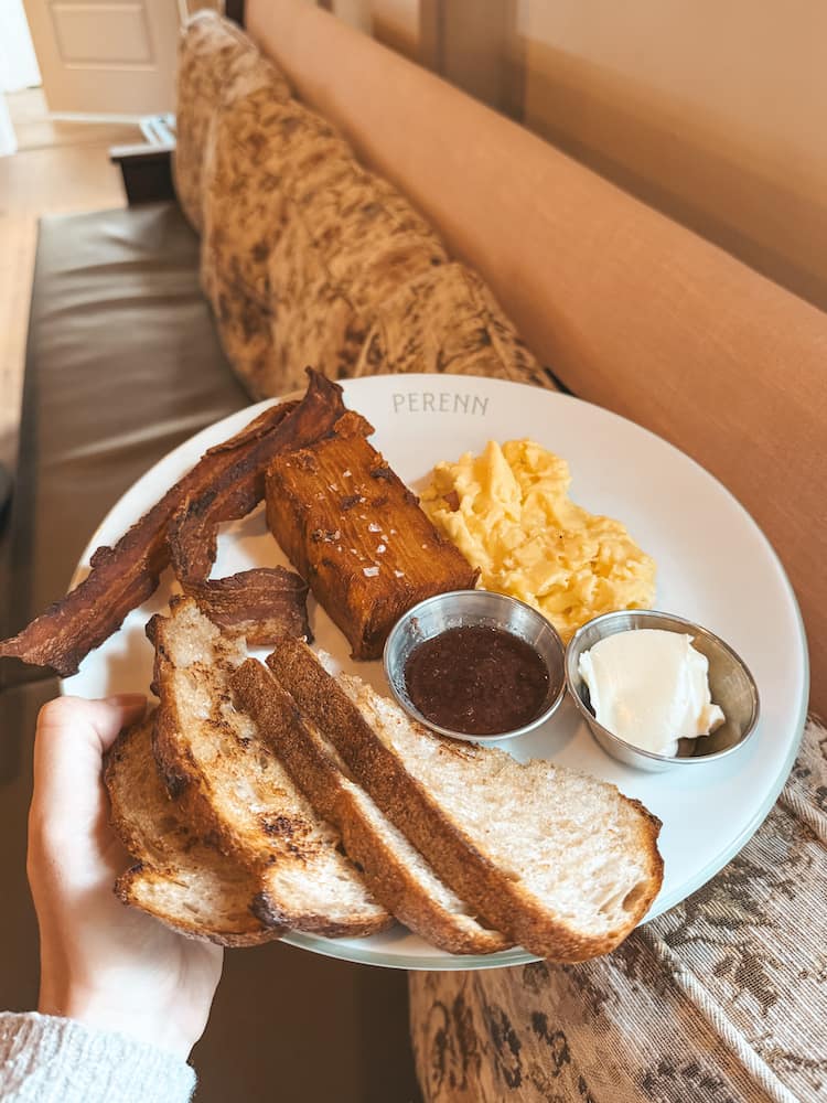 A plate with toast, eggs, bacon, and hashbrowns in front of a booth inside Perenn, one of the best places for brunch in Nashville.