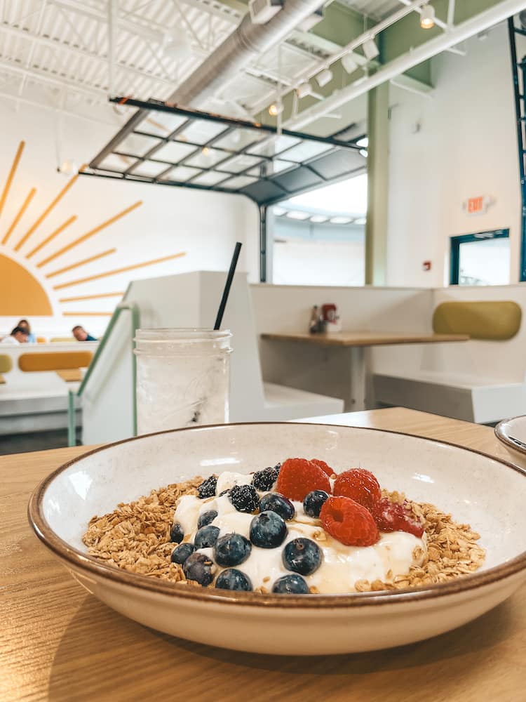 A bowl of granola, yogurt, and fruit sitting on a table in a bright and welcoming brunch restaurant in Nashville.