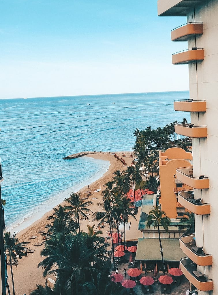 A view of Waikiki Beach's blue water and golden sand with the pink facade of the Royal Hawaiian Resort in the foreground
