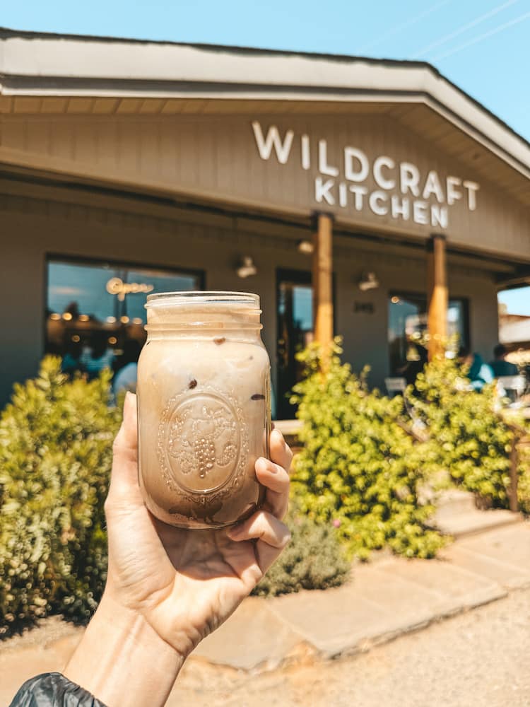 A glass mason jar filled with coffee being held in front of Wildcraft Kitchen in Sedona