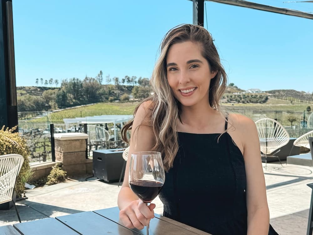 A woman in a black sundress holding a red glass of wine on a patio at one of the best wineries in Temecula.