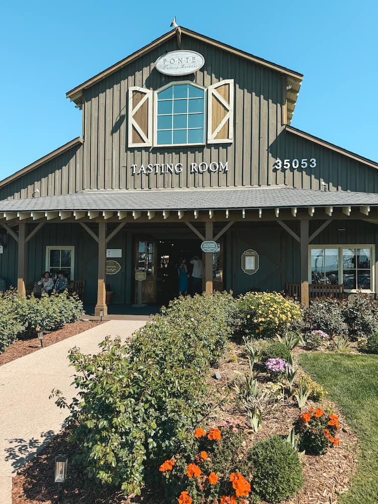The exterior of Ponte Winery in Temecula, housed in a green barn with lush greenery and colorful flowers out front